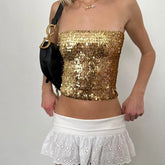 Person wearing a gold sequin top and white skirt with a black handbag - full view